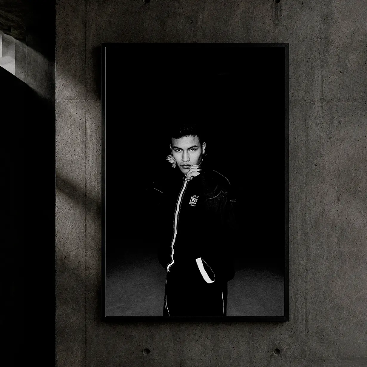 Framed black and white portrait on a concrete wall of a young man in a black bomber jacket under dramatic lighting, fashion photography in Bilbao