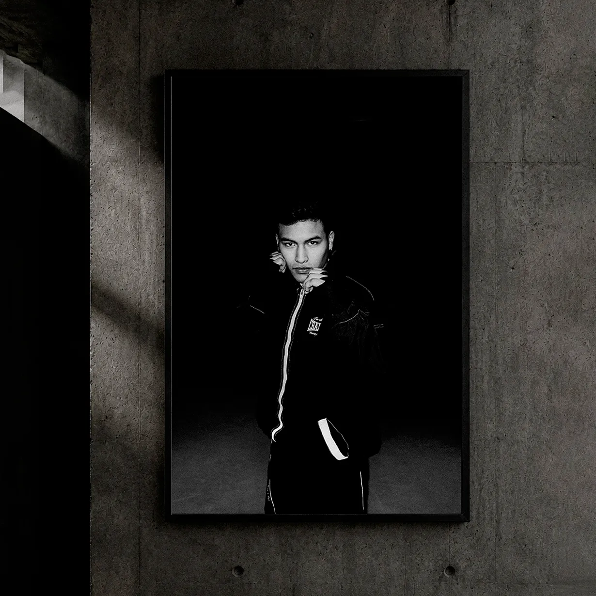 Framed black and white portrait on a concrete wall of a young man in a black bomber jacket under dramatic lighting, fashion photography in Bilbao