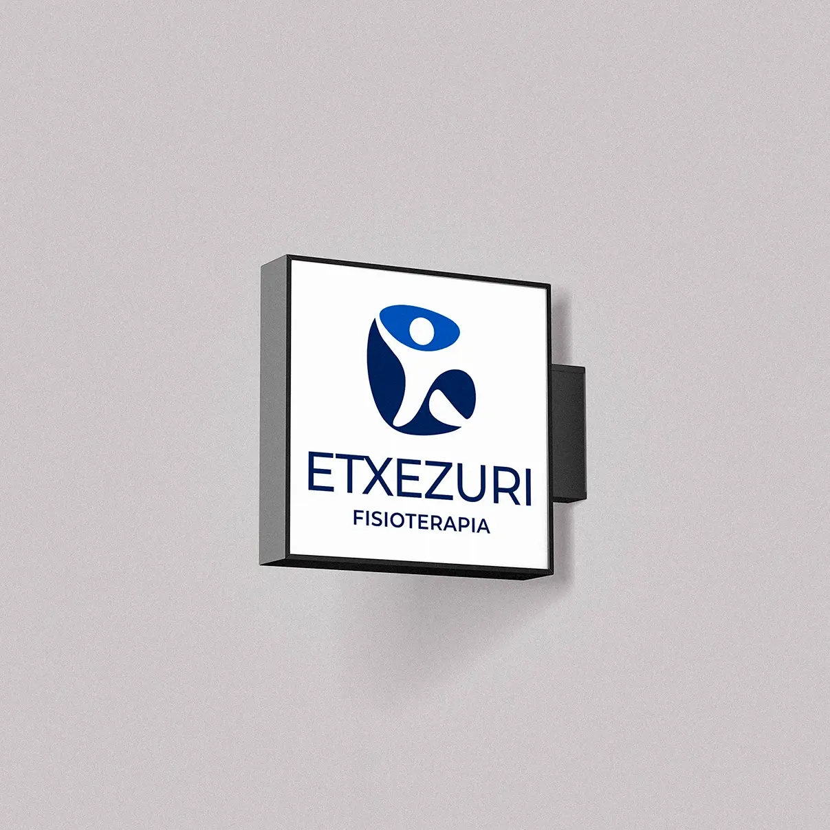 Square illuminated sign for Etxezuri Fisioterapia on a grey facade, with its blue figure logo and navy lettering.