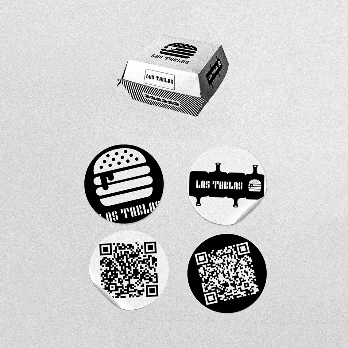 Black and white packaging for the Las Tablas burger joint, with a striped box, logo stickers, a burger icon and QR codes, branding design