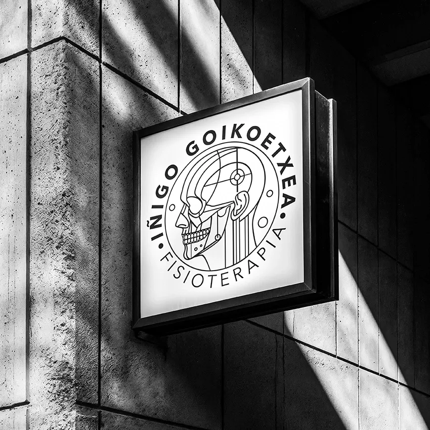Illuminated projecting sign with the circular Iñigo Goikoetxea Fisioterapia logo and a line-art anatomical skull on concrete.