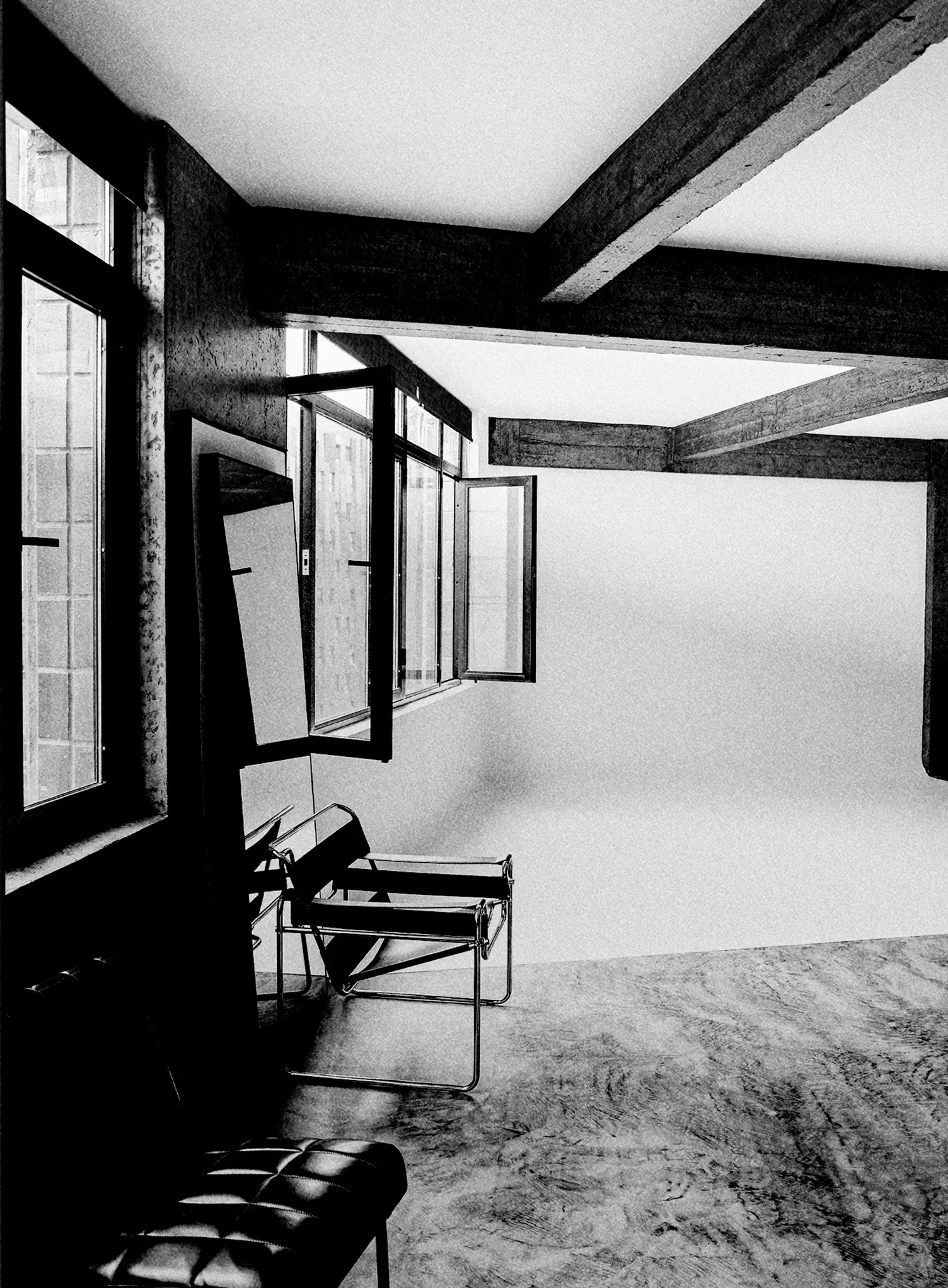 Black and white view of the studio's photography set: a white infinity cyclorama under wooden beams, with large windows and black leather chairs.