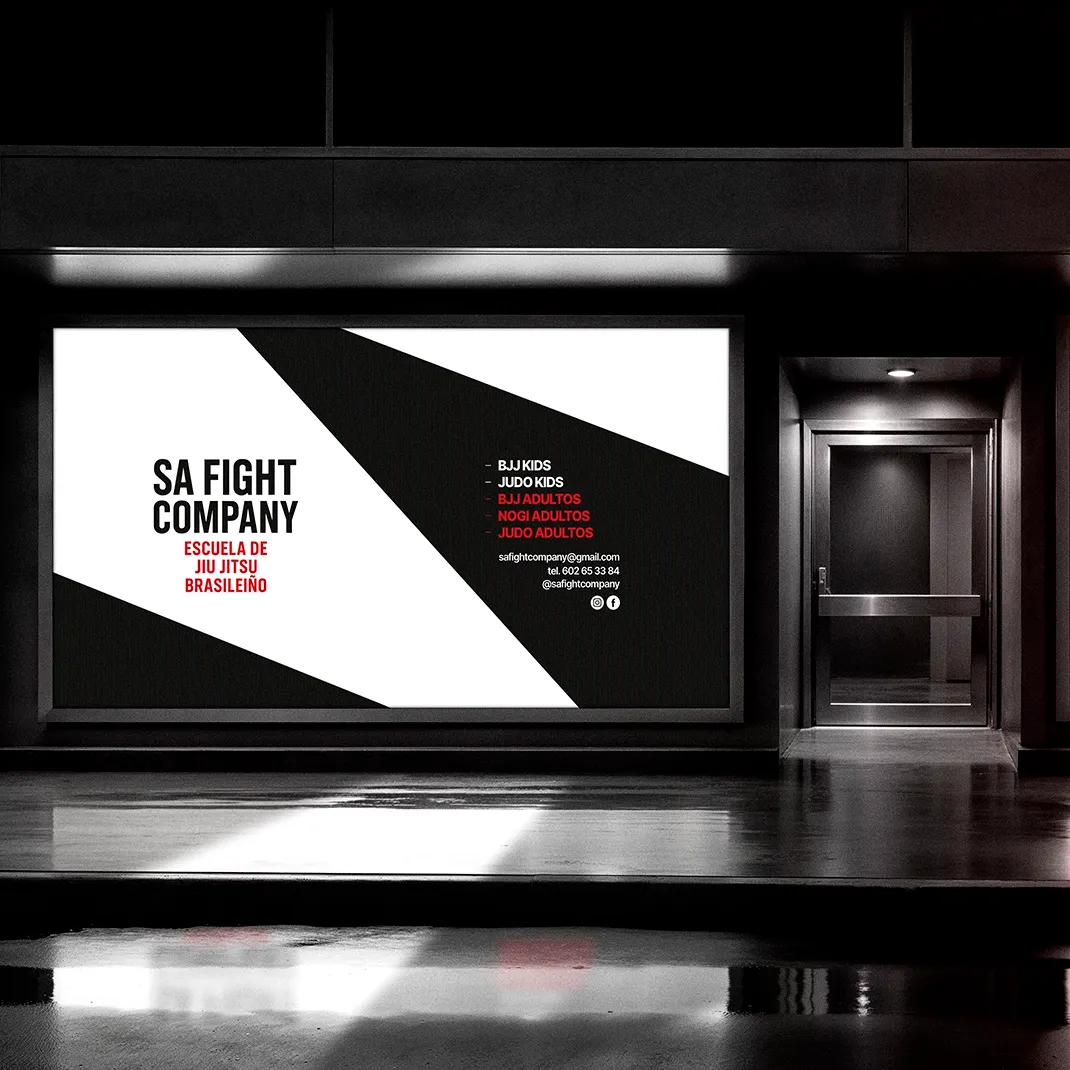 Illuminated storefront window with the SA Fight Company Brazilian jiu jitsu school poster, black and white design listing classes and contact in Bilbao